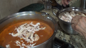 Adding shredded chicken to the mole sauce.