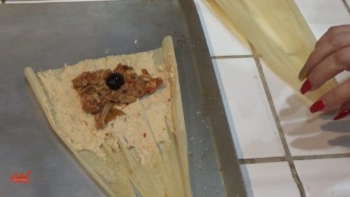 The tamale on the husk, masa, meat or filling, one black olive.